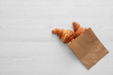 Photo of Paper bag with pastry on light wooden background, top view with space for text