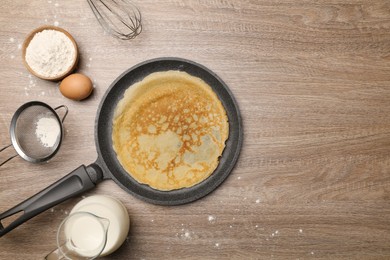 Photo of Frying pan with delicious crepe and ingredients on wooden table, flat lay. Space for text