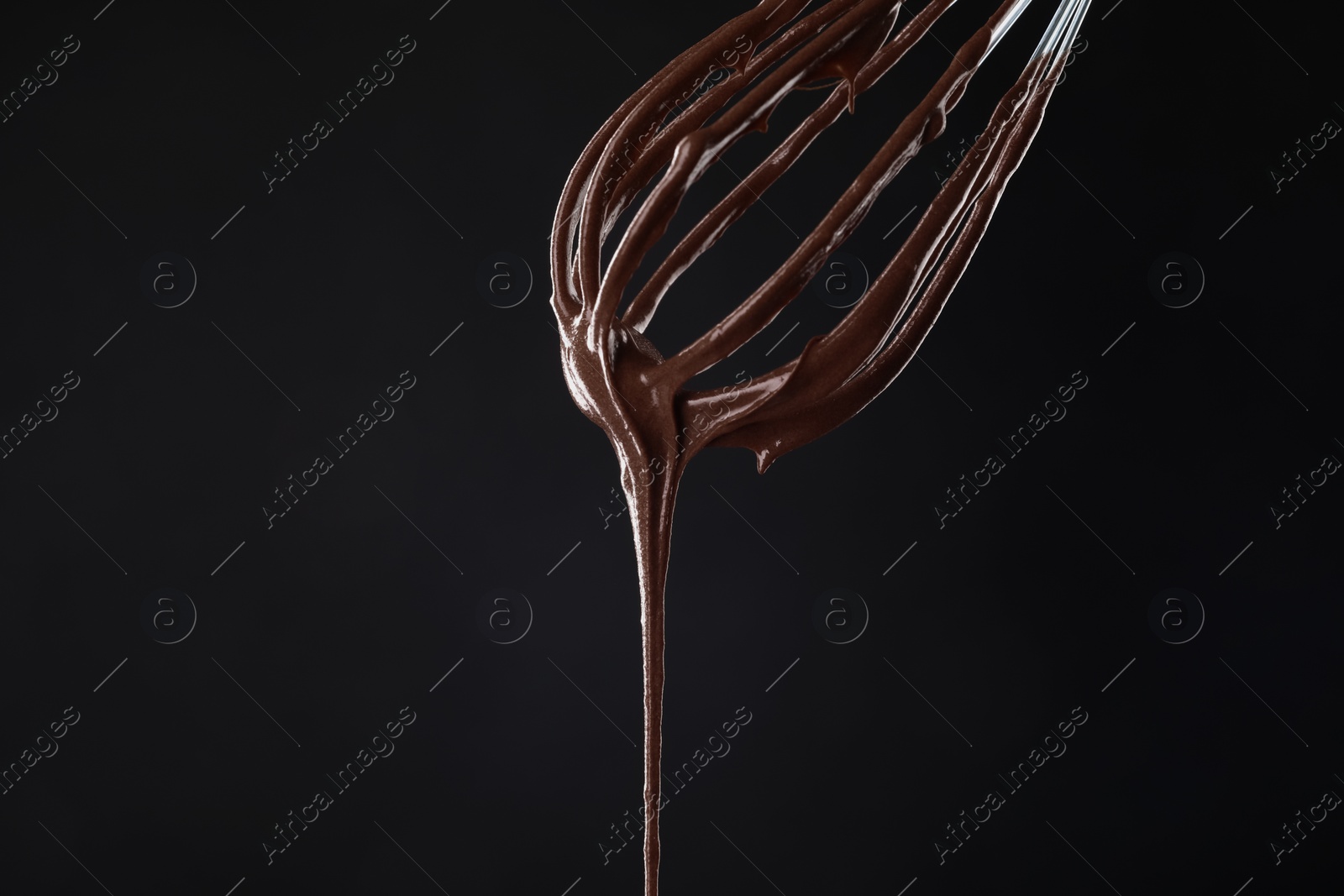 Photo of Chocolate cream flowing from whisk on black background, closeup
