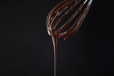 Chocolate cream flowing from whisk on black background, closeup