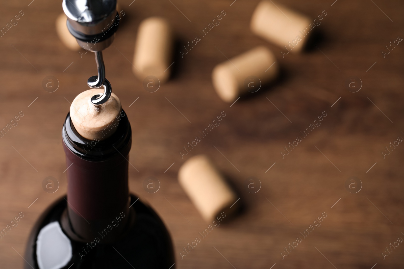 Photo of Opening wine bottle with corkscrew on wooden table, closeup. Space for text