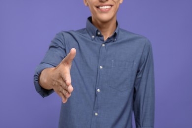 Photo of Happy man welcoming and offering handshake on purple background, selective focus
