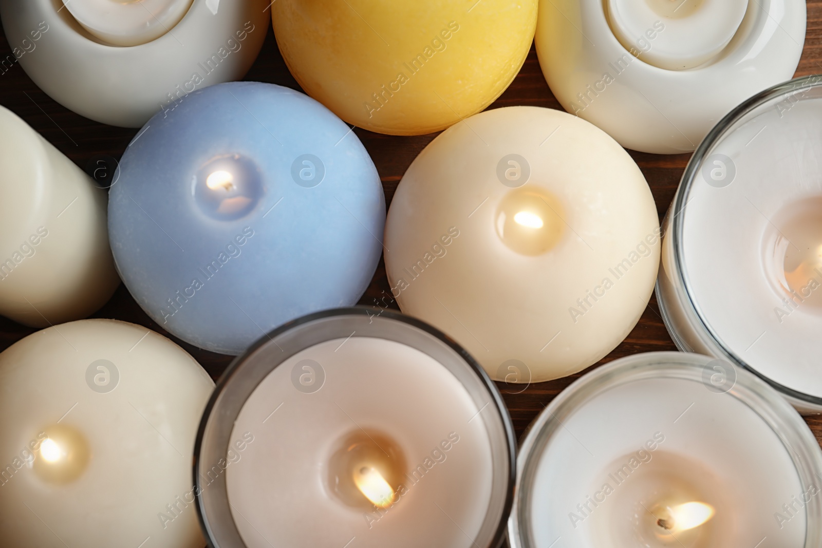 Photo of Burning wax candles of different shapes and colors, top view