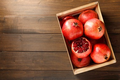Photo of Ripe pomegranates in crate on wooden table, top view. Space for text