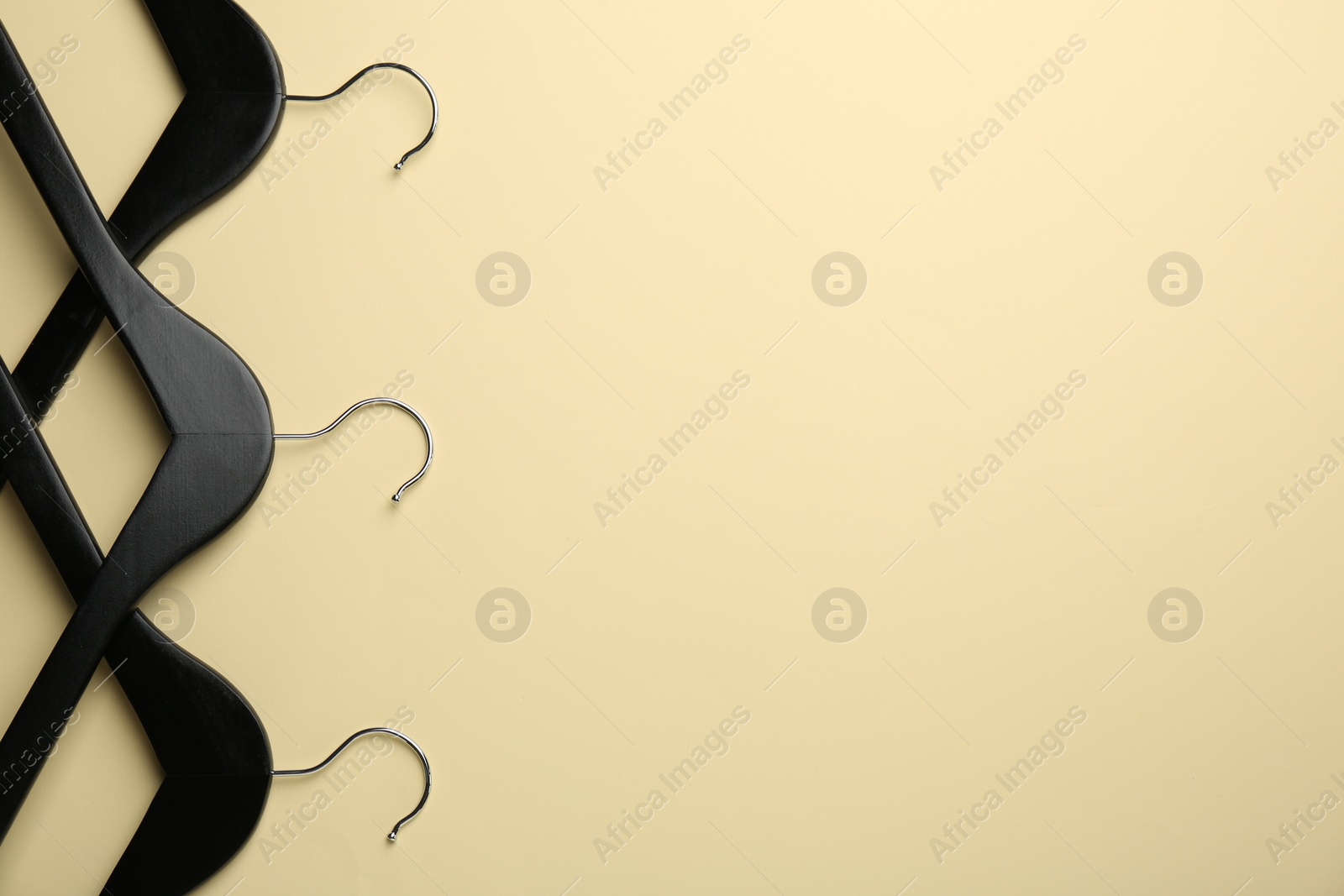Photo of Black hangers on pale yellow background, flat lay. Space for text