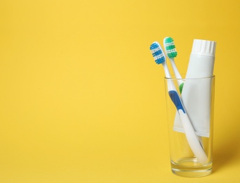 Photo of Glass with brushes and toothpaste on color background. Space for text