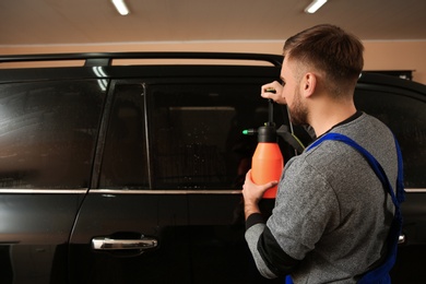 Photo of Skilled worker washing tinted car window in shop