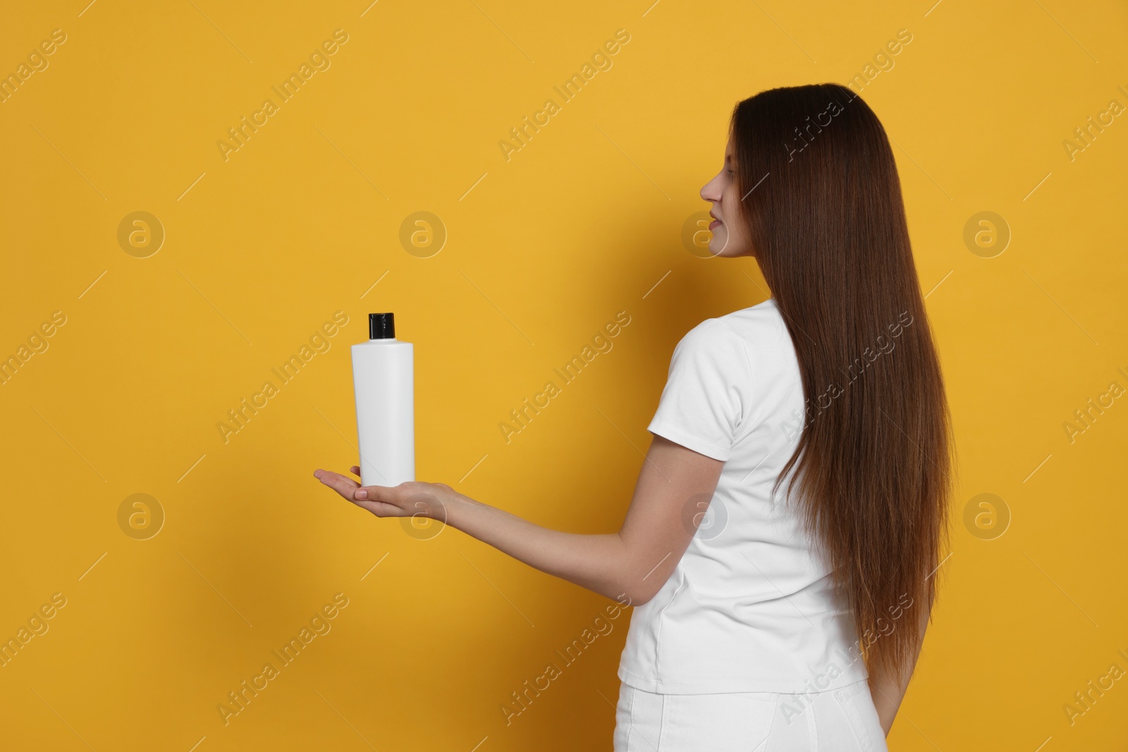 Photo of Beautiful young woman holding bottle of shampoo on yellow background