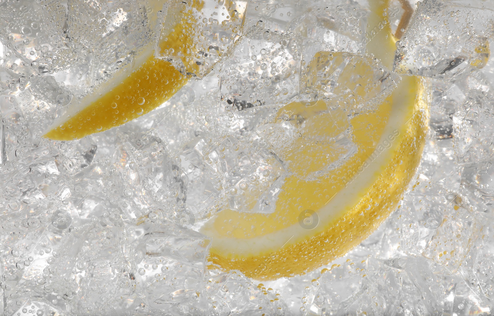 Photo of Juicy lemon slices and ice cubes in soda water against white background, closeup