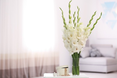 Vase with beautiful white gladiolus flowers and jewellery on wooden table in room, space for text