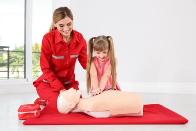 Photo of Instructor with little girl practicing first aid on mannequin indoors