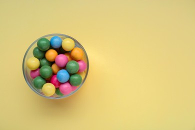 Photo of Bowl with many bright gumballs on beige background, top view. Space for text