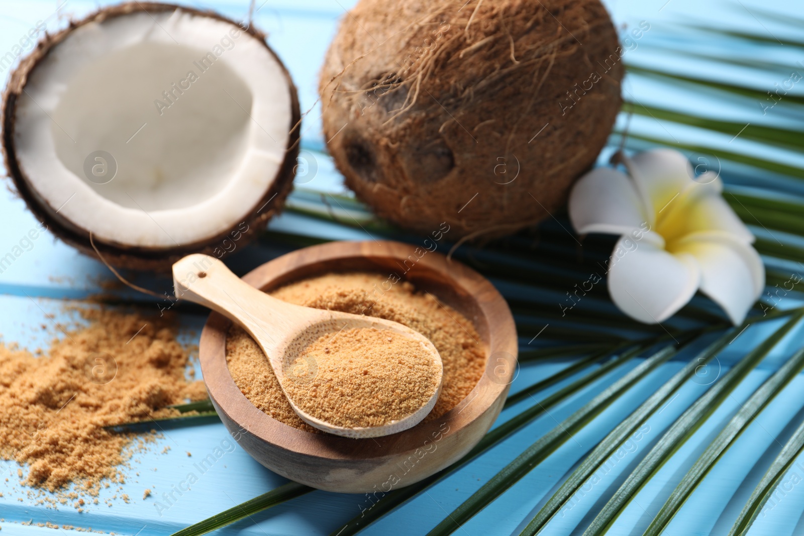 Photo of Coconut sugar, palm leaves, fruits and flower on light blue wooden table, closeup