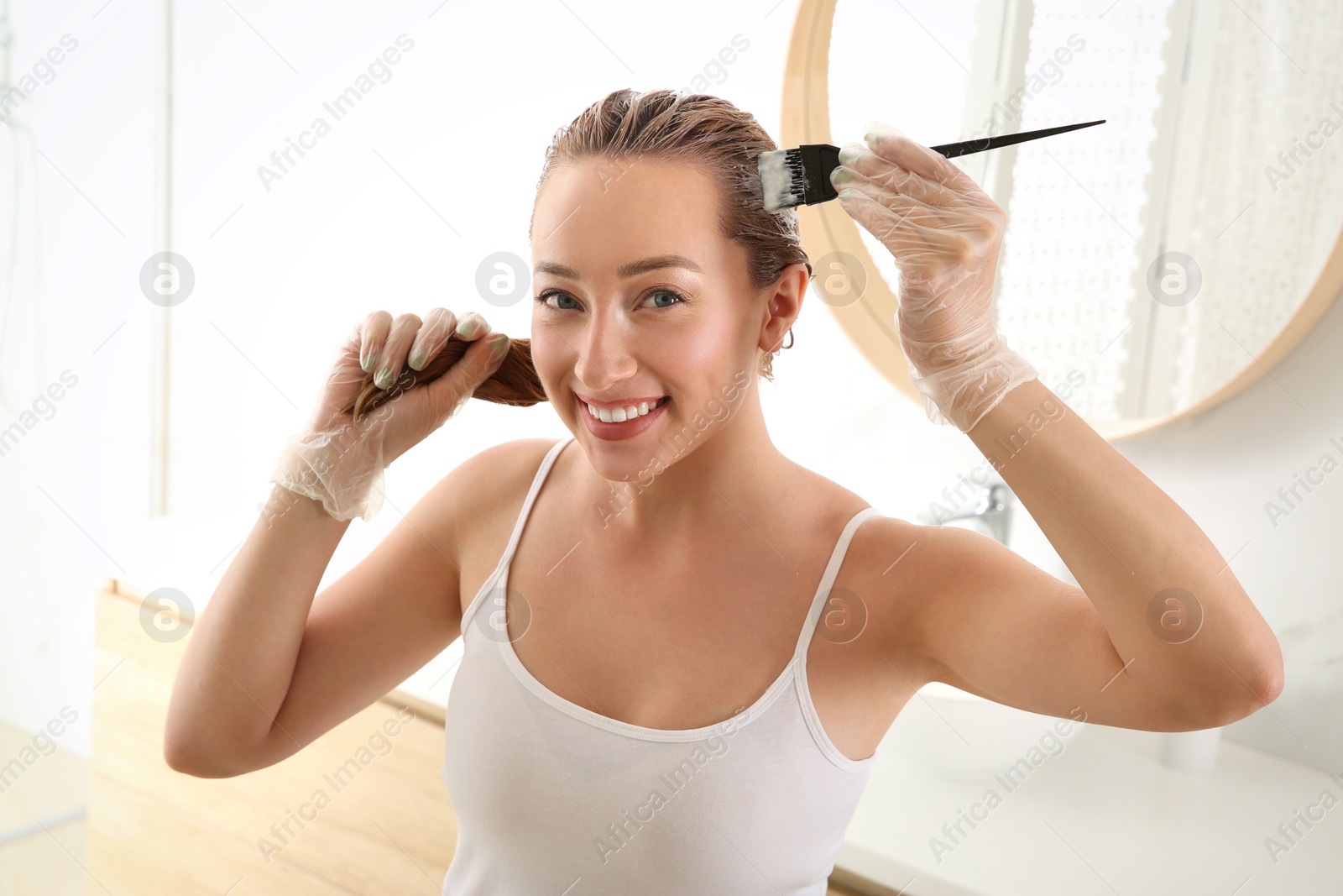 Photo of Young woman dyeing her hair in bathroom