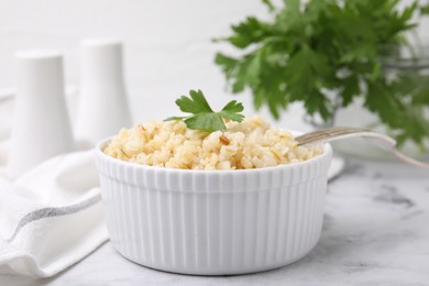 Photo of Cooked bulgur with parsley in bowl on white marble table, closeup