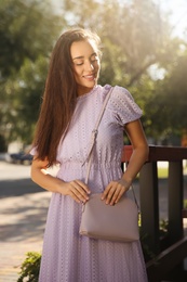 Photo of Beautiful young woman in stylish violet dress with handbag outdoors