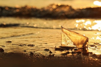 Photo of Used plastic cup on beach at sunset. Space for text