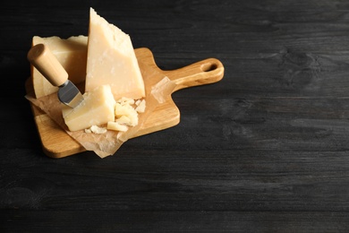 Pieces of Parmesan cheese and knife on black wooden table. Space for text