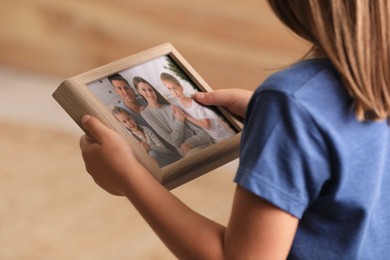 Photo of Little girl holding framed family photo on blurred background, closeup