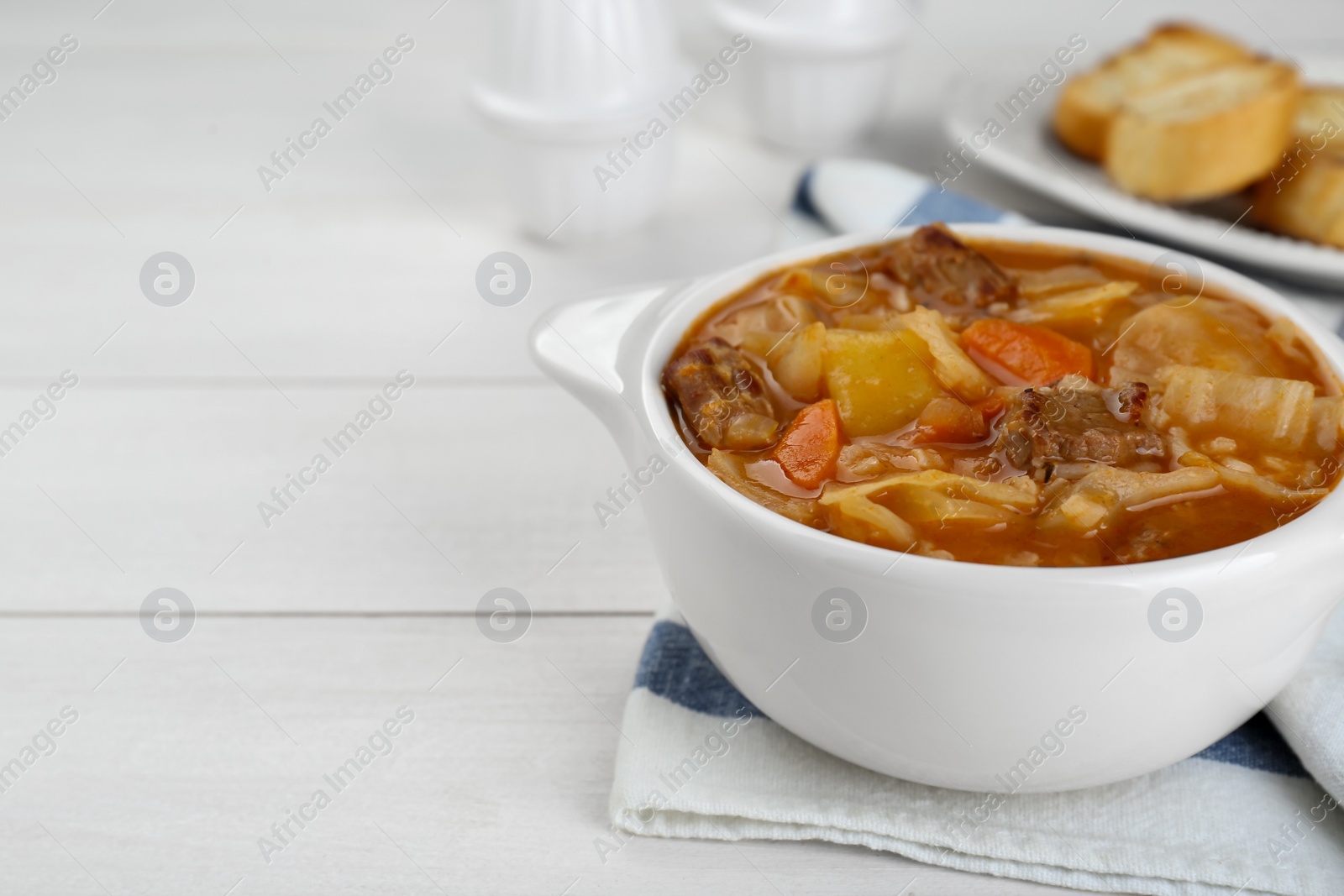 Photo of Tasty cabbage soup with meat and carrot on white wooden table, closeup. Space for text