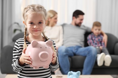 Photo of Family budget. Little girl with piggy bank, her parents and brother at home, selective focus