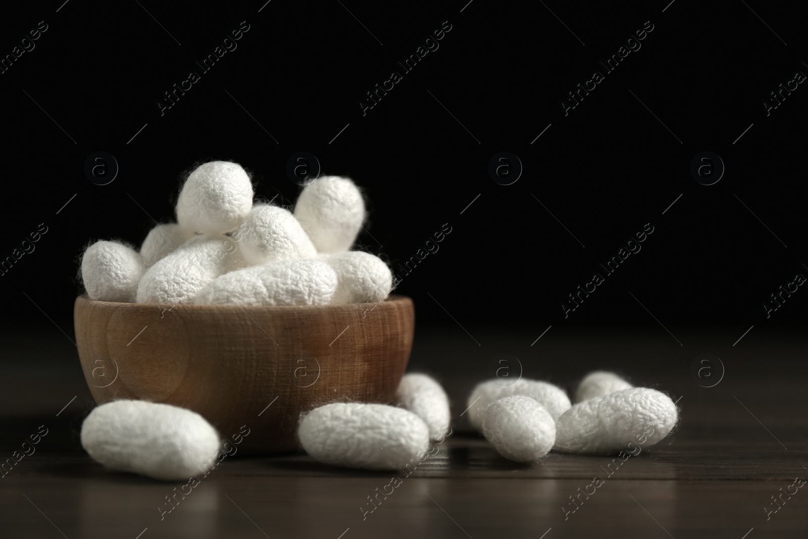 Photo of White silk cocoons with bowl on wooden table, closeup. Space for text