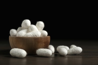 Photo of White silk cocoons with bowl on wooden table, closeup. Space for text