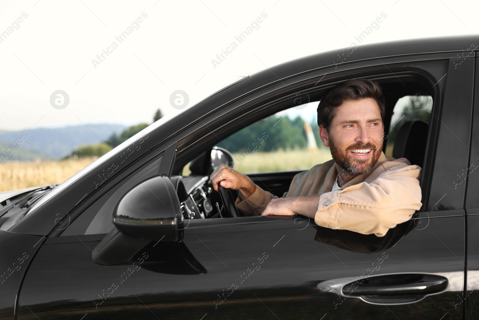 Photo of Enjoying trip. Happy bearded man driving his car, view from outside