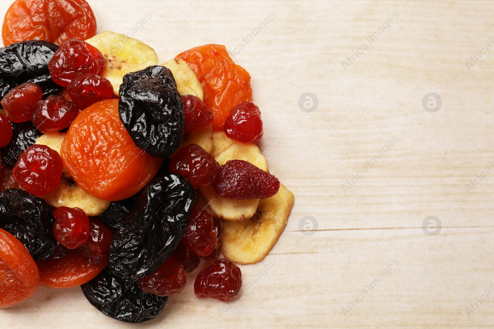 Photo of Mix of delicious dried fruits on white wooden table, top view. Space for text