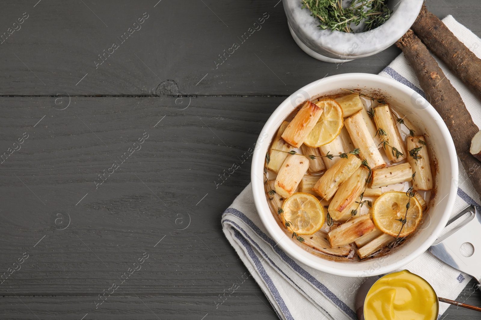 Photo of Dish with baked salsify roots, lemon, thyme and sauce on black wooden table, flat lay. Space for text