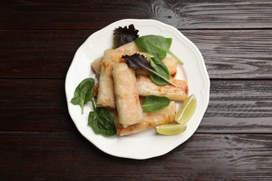Photo of Plate with tasty fried spring rolls, spinach and lime on wooden table, top view