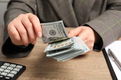 Photo of Money exchange. Woman counting dollar banknotes at wooden table, closeup