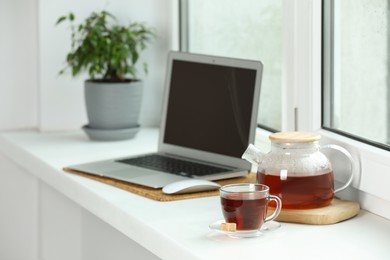 Photo of Modern laptop and tea on white sill near window