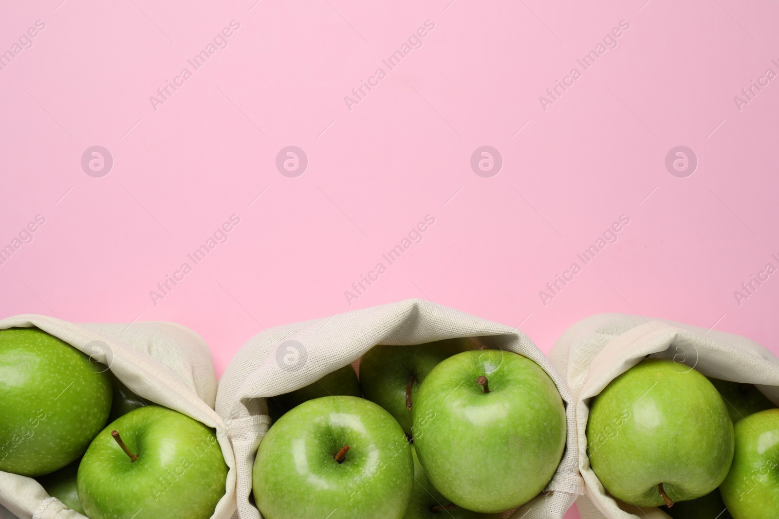 Photo of Sacks with ripe green apples on pink background, flat lay. Space for text