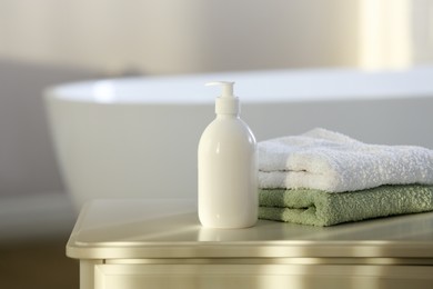 Photo of Bottle of bubble bath and towels on white table in bathroom, space for text
