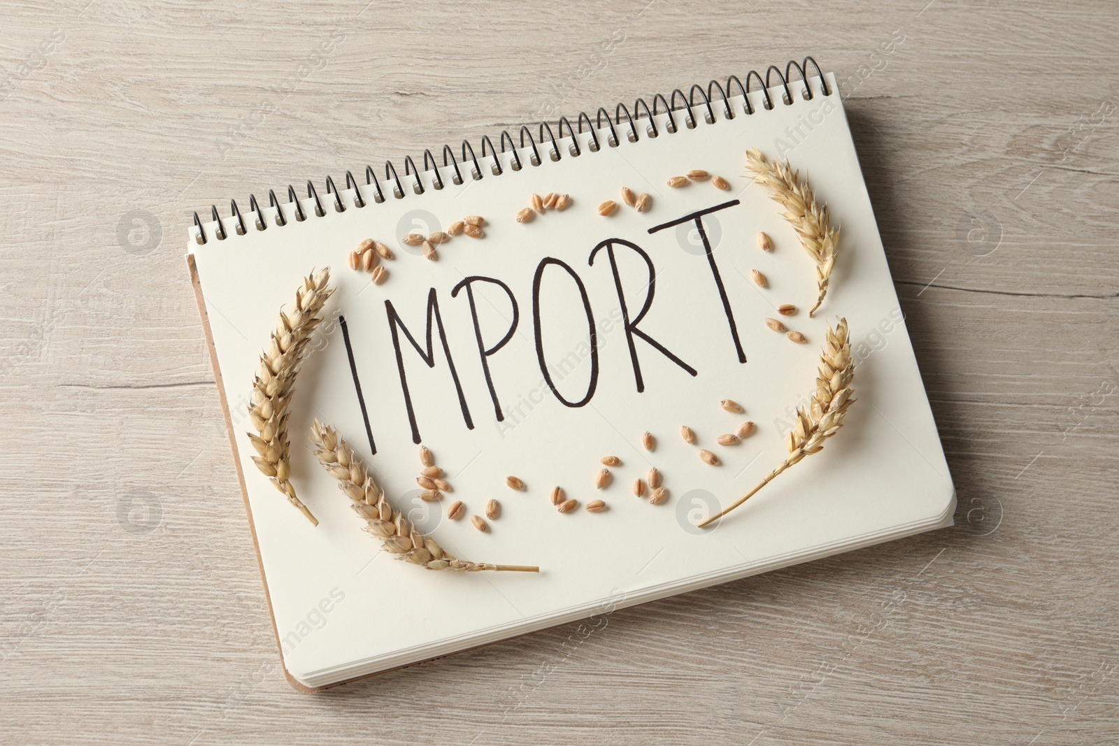 Photo of Notebook with word import and ears of wheat on wooden table, top view