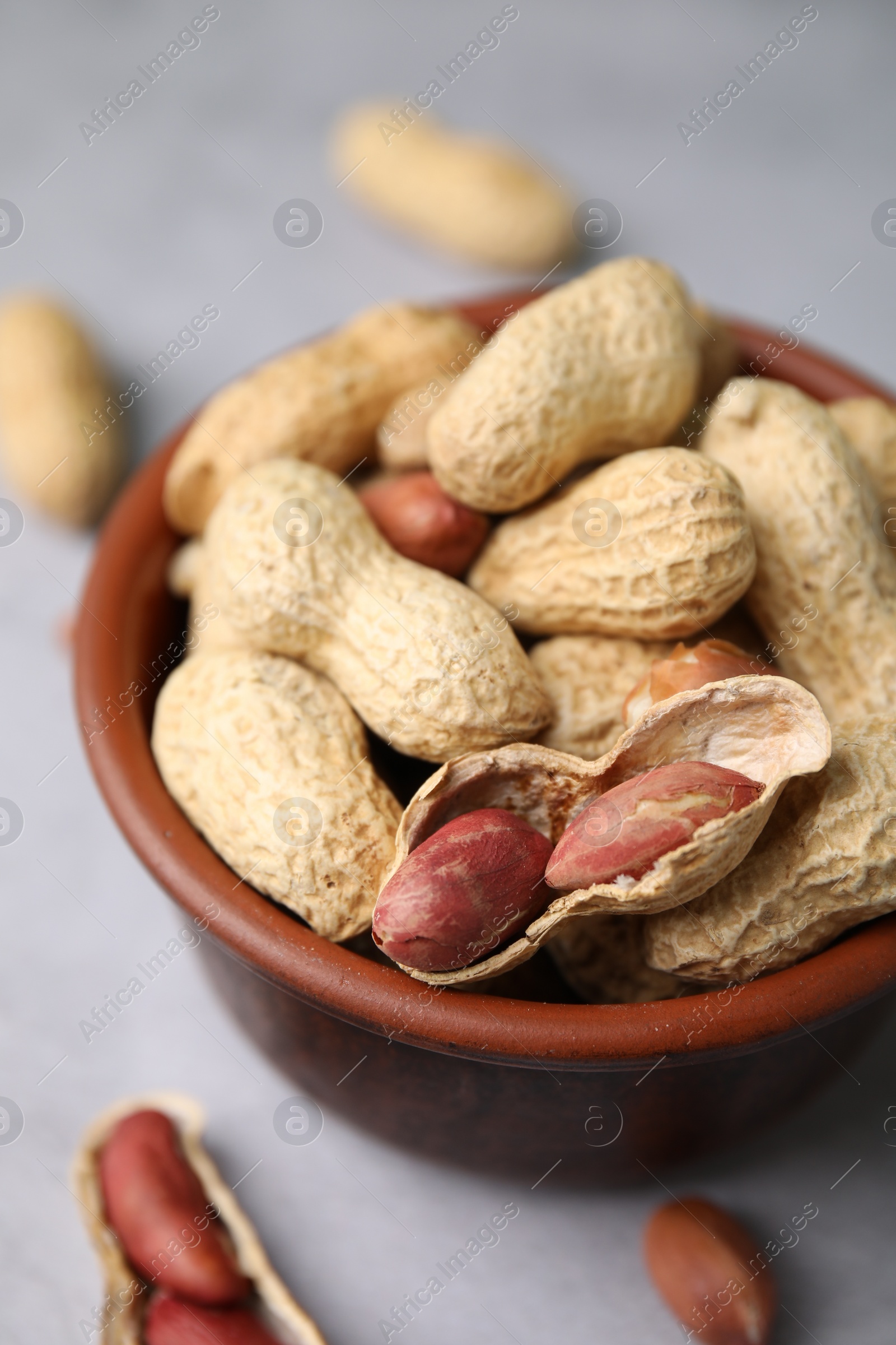 Photo of Fresh unpeeled peanuts in bowl on grey table, closeup