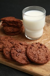 Photo of Board with tasty chocolate cookies and glass of milk on table, closeup