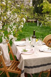 Stylish table setting with beautiful spring flowers, wine, plates and glasses in garden