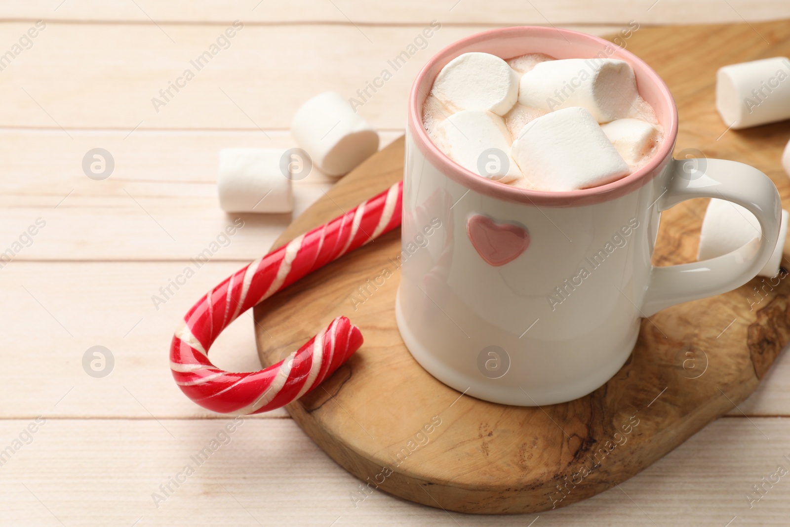 Photo of Tasty hot chocolate with marshmallows and candy cane on light wooden table, closeup. Space for text