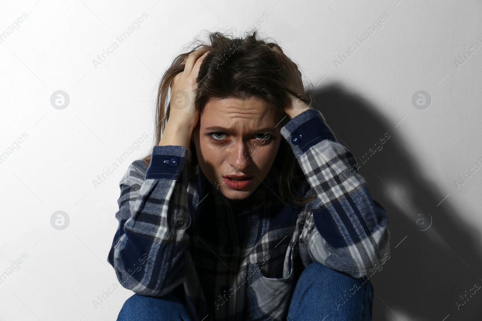 Photo of Abused young woman crying near white wall. Domestic violence concept