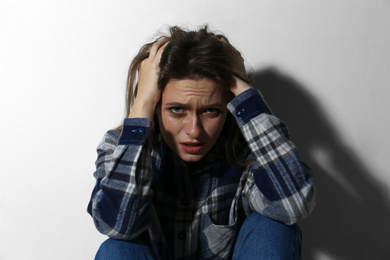 Abused young woman crying near white wall. Domestic violence concept