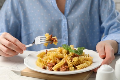 Photo of Woman eating delicious pasta with minced meat and basil at white table, closeup