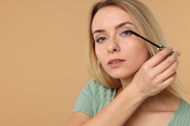 Photo of Beautiful woman applying mascara on beige background. Space for text