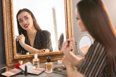 Portrait of beautiful woman with bright makeup near mirror indoors