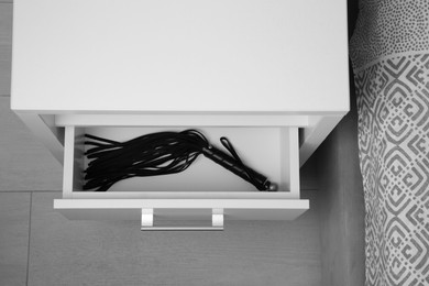Black leather whip in open drawer of bedside table indoors, above view. Sex toy