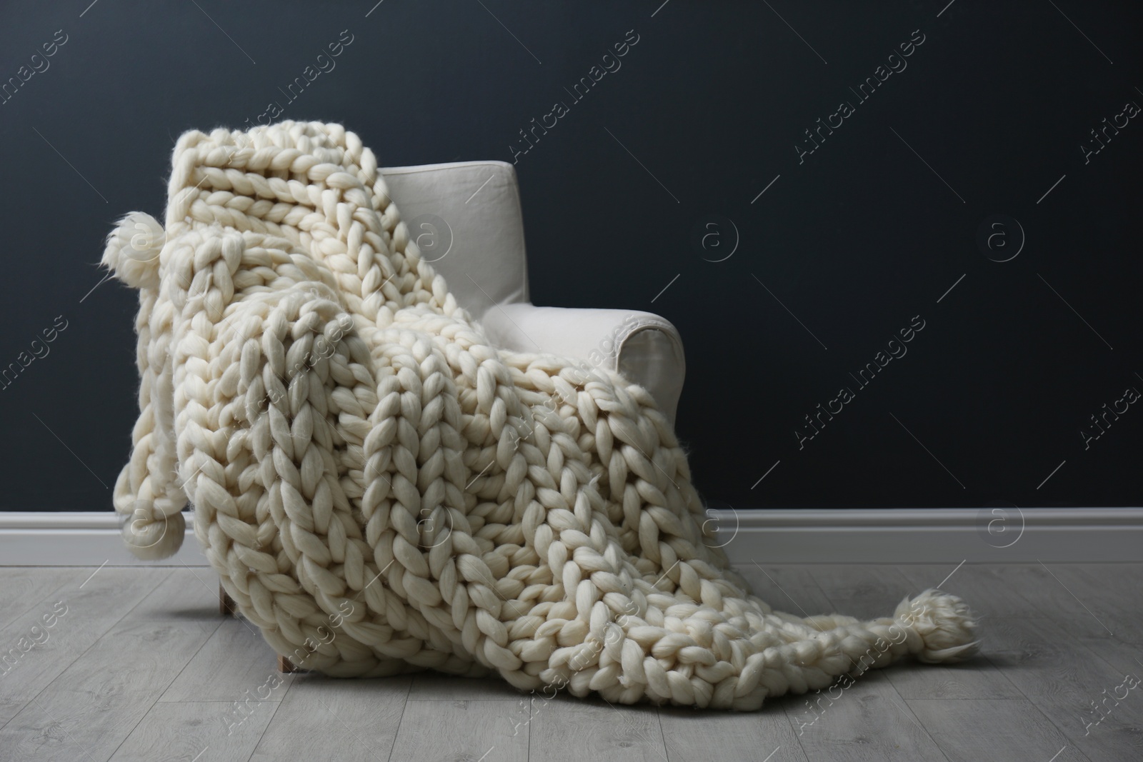 Photo of Soft knitted blanket on armchair in living room. Interior element