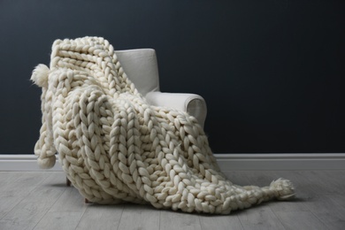 Soft knitted blanket on armchair in living room. Interior element