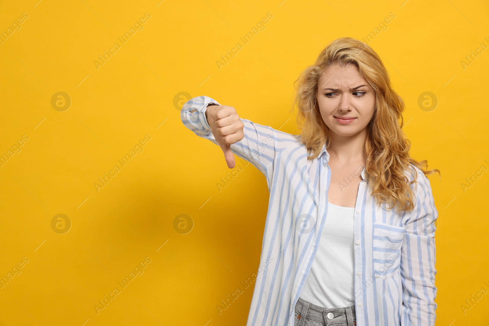 Photo of Dissatisfied young woman showing thumb down gesture on yellow background. Space for text