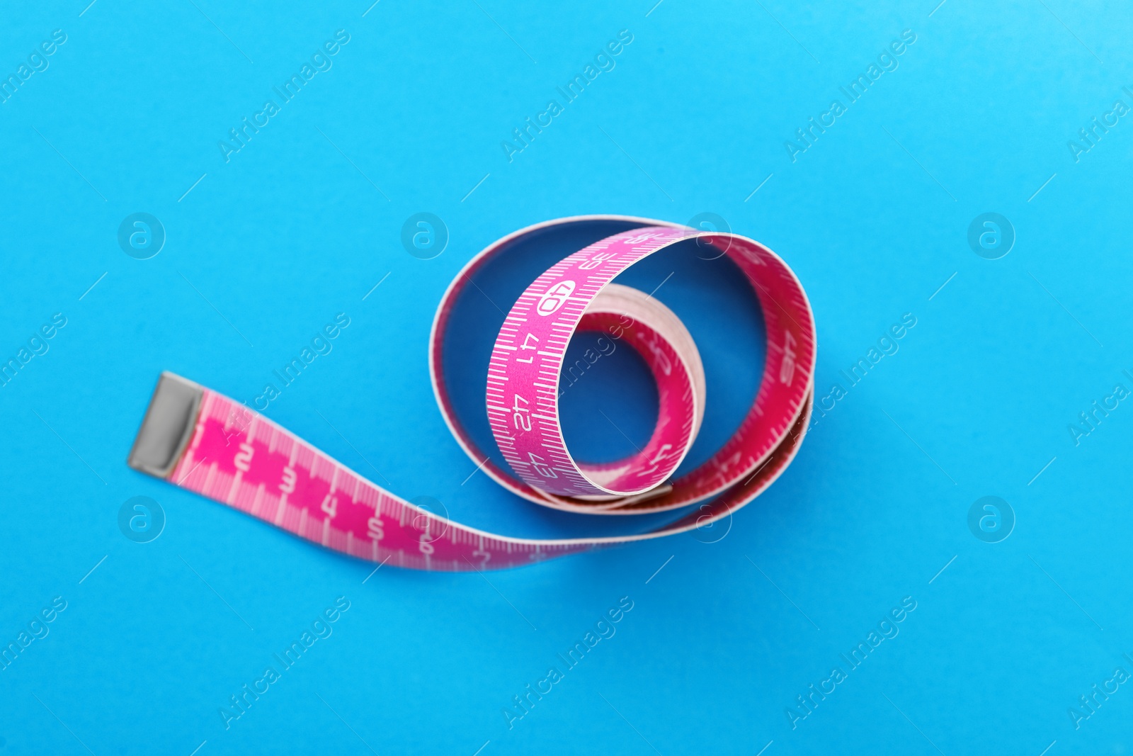 Photo of Pink measuring tape on light blue background, top view